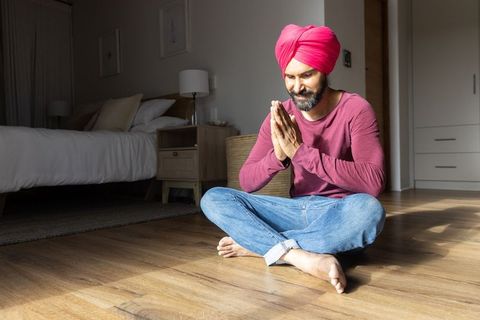 Indian man in pink turban meditating on wooden floor in bedroom