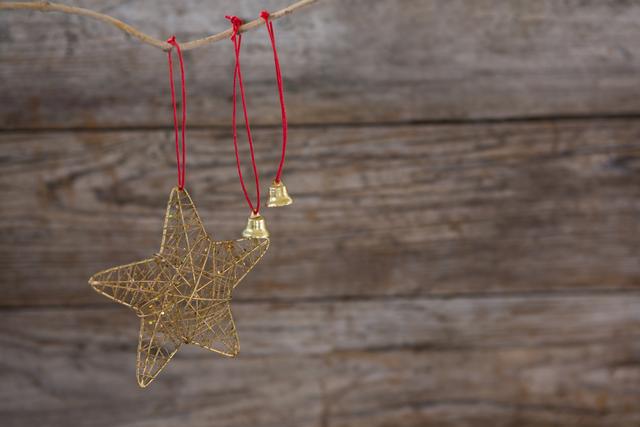 Christmas bell and star ornaments hanging on a branch with red strings against a rustic wooden wall. Perfect for holiday-themed designs, greeting cards, festive advertisements, and seasonal blog posts.