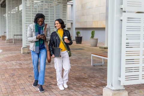 Walking and chatting on urban brick plaza under louvered pergola holding coffee and phone