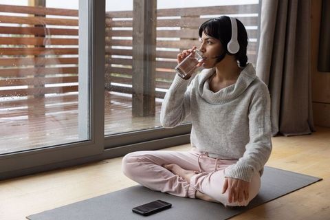Woman relaxing on yoga mat with headphones and water