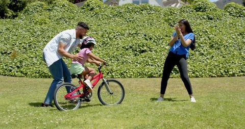Hispanic Family Guiding Young Girl Riding Bicycle Outdoors