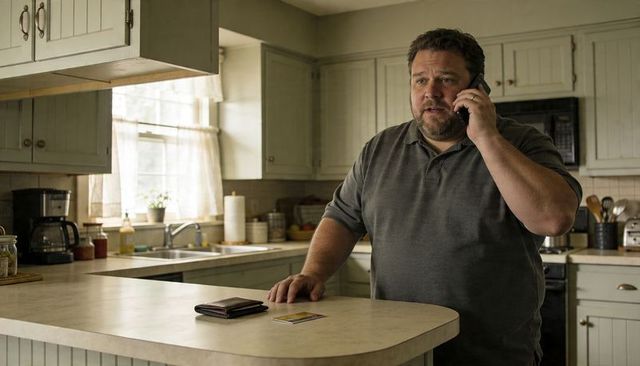 Man talking on phone at kitchen island with wallet and credit card on counter