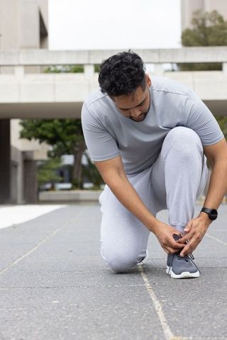 Man kneeling tying running shoe on urban plaza preparing for outdoor workout