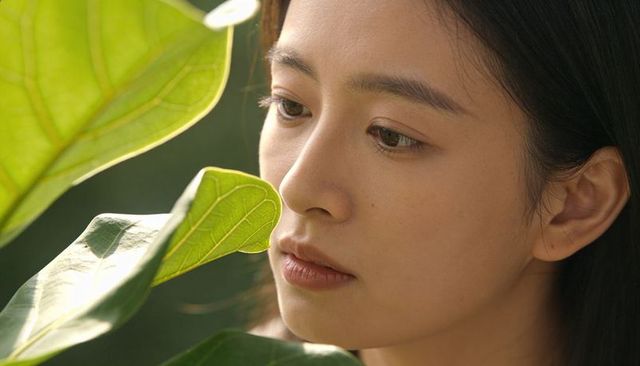 Gazing asian woman leaning toward veined green leaf closeup portrait in natural light