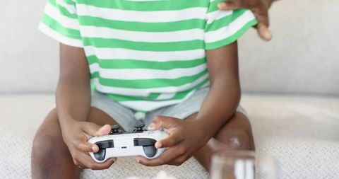 African american boy playing video game with parent, family bonding on sofa