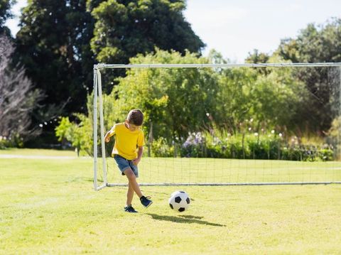 Boy kicking soccer ball toward goal on grassy field