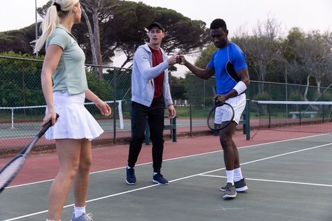 Diverse tennis teammates exchanging fist-bump on outdoor court demonstrating teamwork