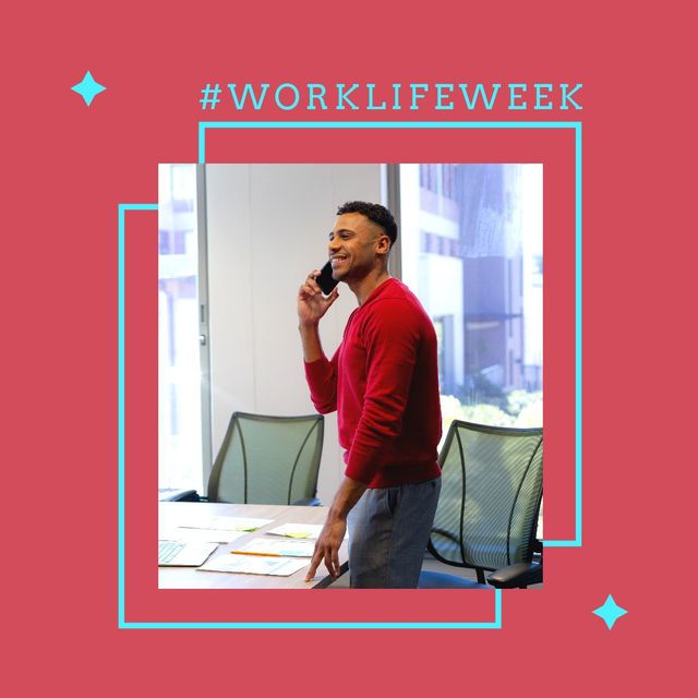 This image of a happy biracial man using a smartphone while standing in a modern office celebrates National Work Life Week. It can be used for promoting workplace well-being, work-life balance initiatives, corporate programs, and diversity in the workplace.
