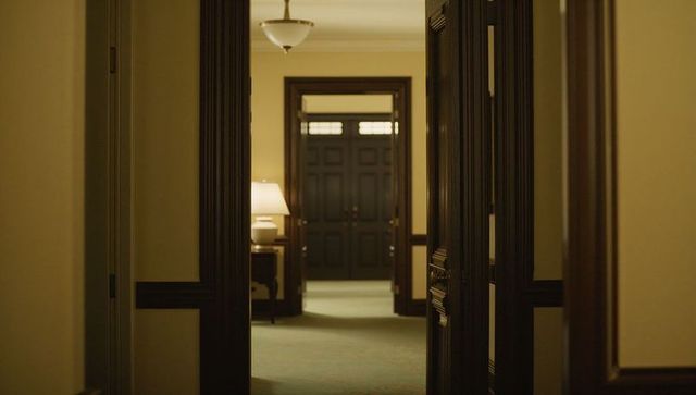Framing ornate dark-wood double doors leading down elegant foyer with warm lamp light