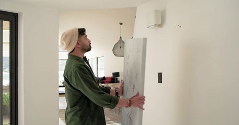 Indian man hanging large abstract canvas in modern minimalist home hallway