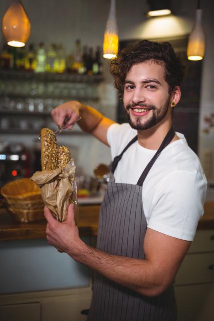 This image is ideal for use in marketing materials for cafés, bakeries, or hospitality services. It can be used in advertisements, websites, or social media posts to highlight friendly customer service and fresh baked goods. The cheerful demeanor of the waiter adds a welcoming and approachable feel, making it perfect for promoting a positive dining experience.