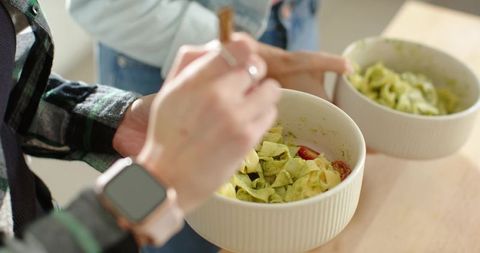 Friends sharing homemade pesto pasta in ceramic bowls rustic kitchen closeup rose gold watch