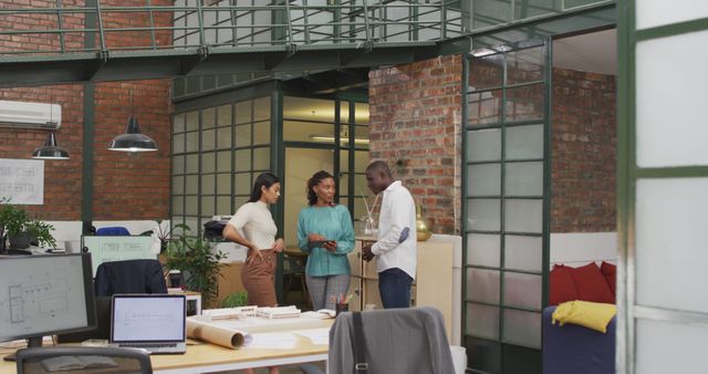 Group of architects working together in a modern, open-space office with an industrial design. Perfect for illustrating concepts of teamwork, creative work environments, consulting, and engineering projects. Useful for articles or marketing materials focusing on architecture, office culture, or team collaboration.