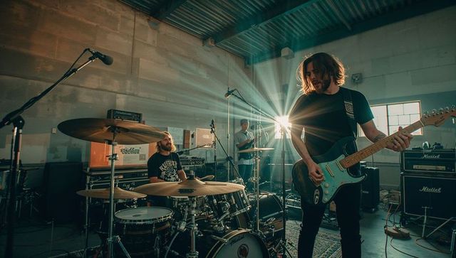Garage rock band rehearsing with electric guitar and drum kit, backlit sunburst lens flare