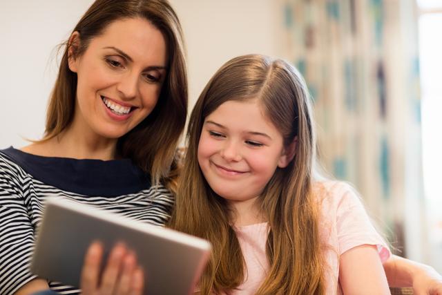 Mother and daughter using digital tablet in living room at home