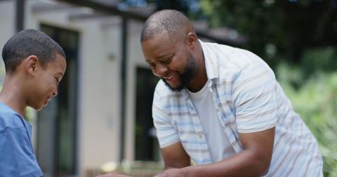 African american father teaching son in backyard patio, sharing hands-on moment smiling