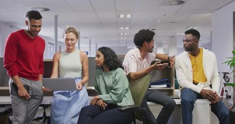 Diverse team collaborating around laptop in modern open office, informal presentation