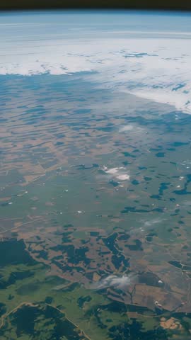 Vertical aerial footage drifting over patchwork farmland and lakes toward distant horizon