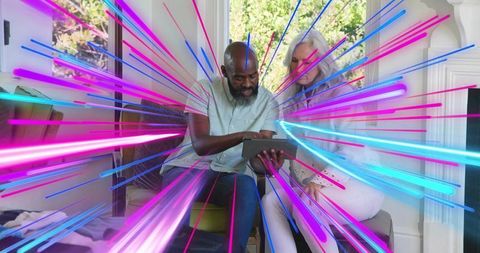 Senior couple holding tablet in cozy living room with neon tech streaks radiating