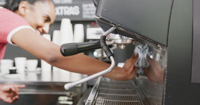 Barista maintaining cleanliness by wiping down an espresso machine in a coffee shop environment. This image is ideal for use in topics related to barista training, coffee shop hygiene standards, hospitality industry practices, or promotional materials for cafes and coffee-related businesses.