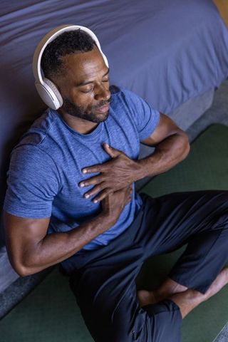 African american man meditating with headphones on bedroom floor mat practicing mindfulness