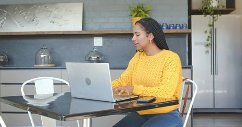 African american woman working on laptop in modern cafe kitchen wearing yellow sweater