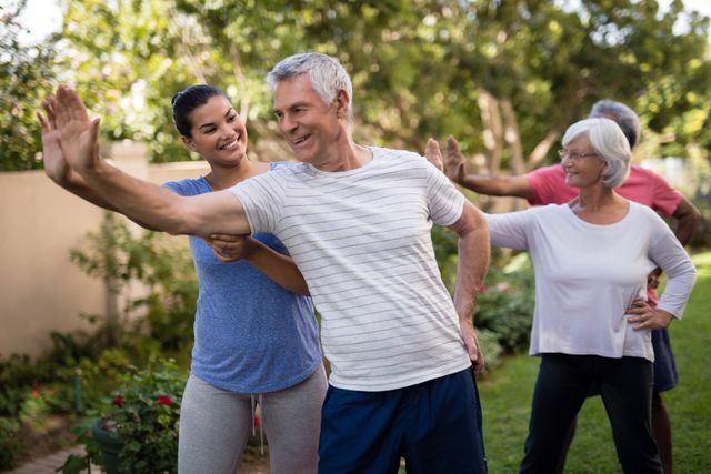 Group of senior individuals engaging in a fitness class led by a cheerful trainer in a park. Ideal for promoting senior health, outdoor fitness programs, and active lifestyles for older adults. Useful for websites, brochures, and advertisements focused on wellness, fitness, and healthy living for seniors.