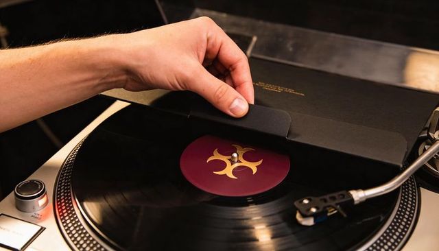 Hand lifting vinyl sleeve from silver turntable, revealing tonearm and retro record