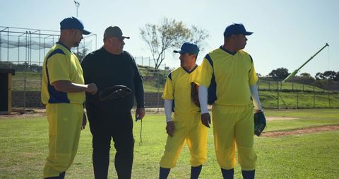 Umpire and players discussing strategy on sunny ballfield wearing yellow uniforms