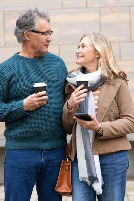 Mature couple enjoying coffee and conversation on city sidewalk, casual autumn attire