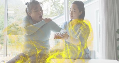 Caregiver checking pulse of woman on sunlit sofa during home care visit, empathy moment