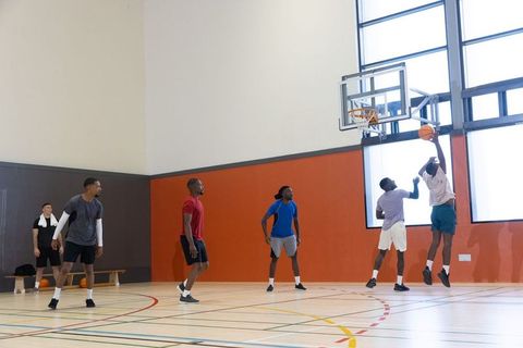 Diverse male teammates contesting rebound during intense indoor basketball play in gym