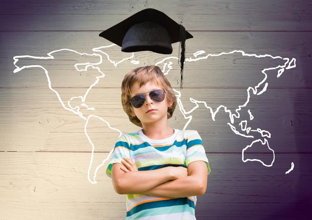 A young boy wearing sunglasses stands confidently with arms crossed in front of a wooden wall featuring a world map and a digitally illustrated graduation cap above his head. This image can be used for educational materials, advertisements for academic programs, or motivational content aimed at young students.