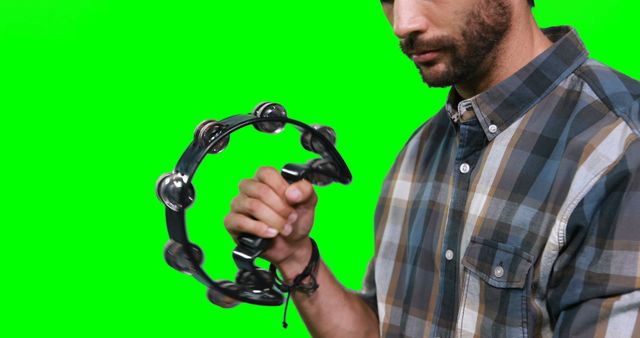 Man holding and playing tambourine against green screen background. Green screen allows easy editing and layering for various multimedia projects, perfect for musical performance videos, tutorial content, or educational purposes.