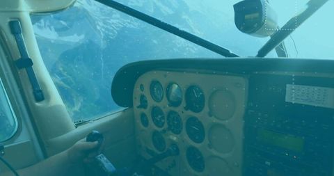 Pilot gripping yoke over snow-capped mountains in cockpit with analog instruments