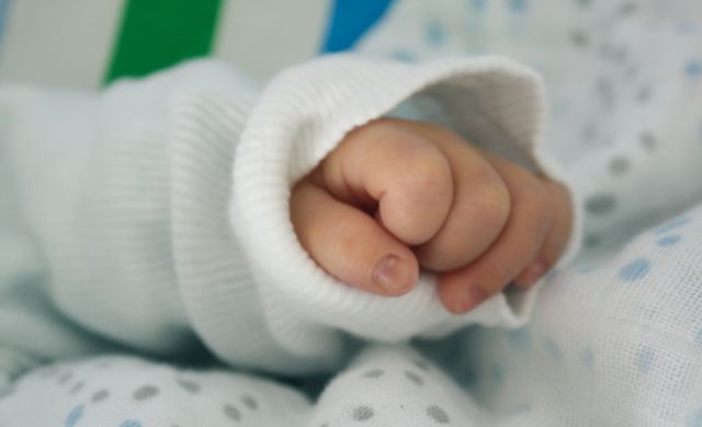 Close-up of a newborn baby's hand gently wrapped in a soft blanket. Perfect for illustrating themes of motherhood, infancy, and early development. Useful for parenting blogs, baby product advertisements, and hospital maternity ward promotions.