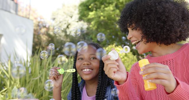 A joyful moment of a woman and her daughter happily blowing soap bubbles together in a lush green garden under the sun. Ideal for family-oriented content, parenting articles, advertisements focused on outdoor activities, and lifestyle blogs. Demonstrates themes of bonding, fun, and creating lasting memories.