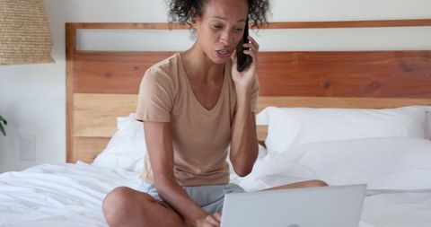 Woman multitasking with phone and laptop in minimalist bedroom