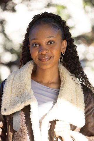 Sunlit african woman wearing shearling leather jacket smiling and holding bag strap