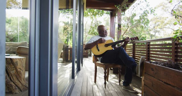 Thoughtful african american senior man sitting on balcony playing acoustic guitar - Download Free Stock Photos Pikwizard.com