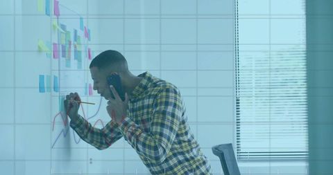 Man in Plaid Shirt Innovating with Graph on Glass Wall in Modern Office