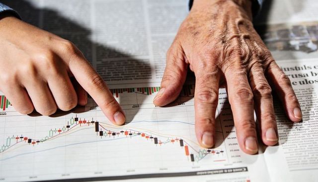 Senior and young hands pointing at declining candlestick chart illustrating market loss