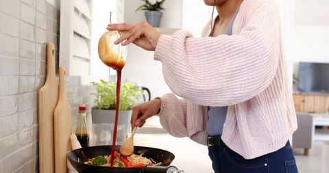 Woman Preparing Stir-Fry Noodles with Sauce in Modern Kitchen
