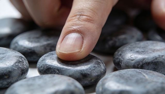 Pressing fingertip on polished basalt spa stones close-up