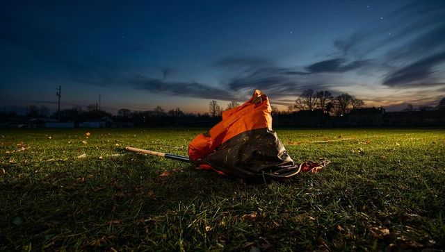 Lying orange-and-black flag collapsing on grass at dusk with dramatic twilight sky