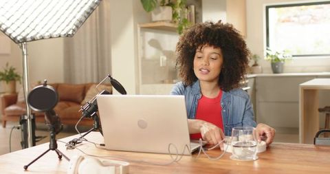 Recording home podcast: woman hosting live stream with laptop, microphone, studio light