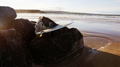 Surfboard Resting on Sharp Rock at Sunny Beach Riptide