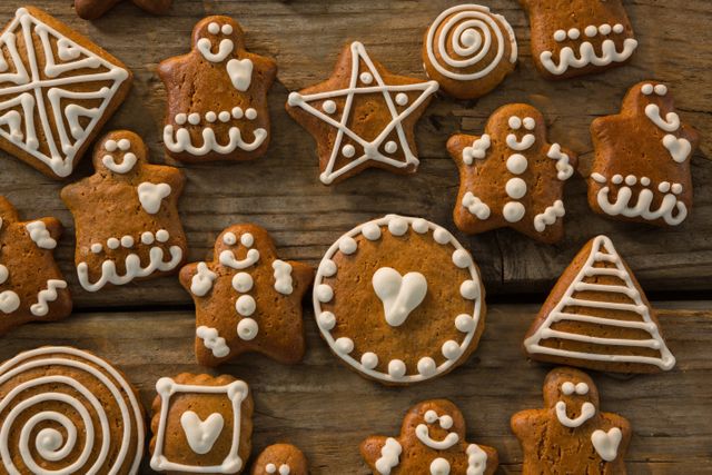 Assorted gingerbread cookies decorated with white icing are arranged on a rustic wooden table. This image is perfect for holiday-themed projects, baking blogs, festive greeting cards, and culinary magazines. It evokes a warm, cozy feeling ideal for Christmas and winter celebrations.