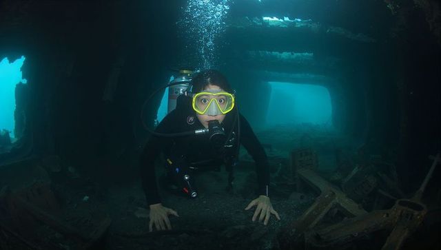 Scuba diver exploring sunken shipwreck interior wearing yellow mask and full scuba gear
