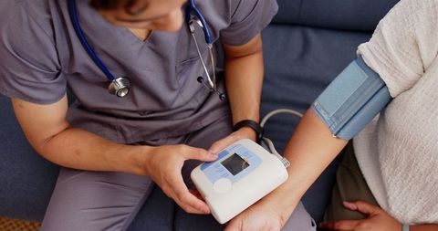 Healthcare worker measuring senior woman's blood pressure with device